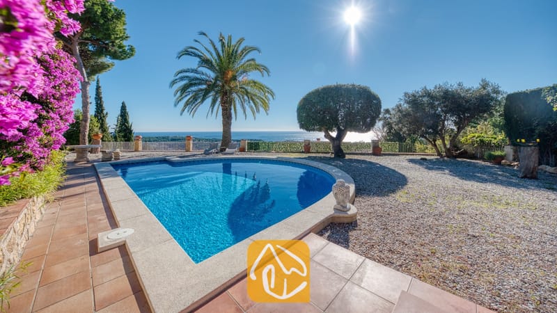 Vakantievilla's Costa Brava Spanje - Villa Gabriella - Privézwembad bij Villa Gabriella met uitzicht op zee, een palmboom en een stenen Boeddhabeeld op het betegelde terras.