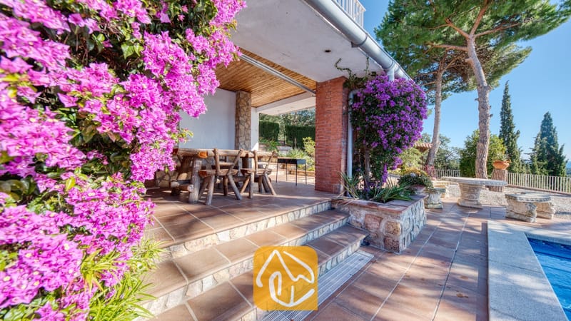 Vakantievilla's Costa Brava Spanje - Villa Gabriella - Overdekt terras bij Villa Gabriella met een rustieke houten eethoek, roze bougainvillea en betegelde trappen die uitkijken over een tuin.