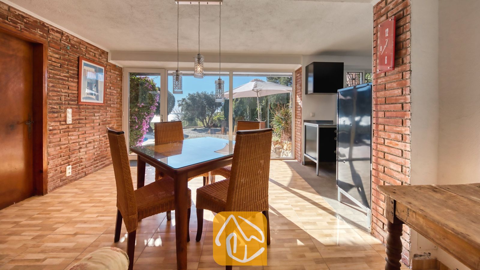Vakantievilla's Costa Brava Spanje - Villa Gabriella - Eetkamer met een glazen tafel en rieten stoelen, sfeervol geplaatst tegen muren van rode baksteen. Grote schuifdeuren bieden een prachtig uitzicht op de tuin en het buitenterras van Villa Gabriella.