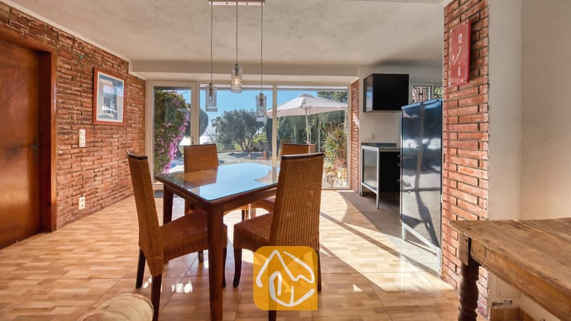 Vakantievilla's Costa Brava Spanje - Villa Gabriella - Eetkamer met een glazen tafel en rieten stoelen, sfeervol geplaatst tegen muren van rode baksteen. Grote schuifdeuren bieden een prachtig uitzicht op de tuin en het buitenterras van Villa Gabriella.