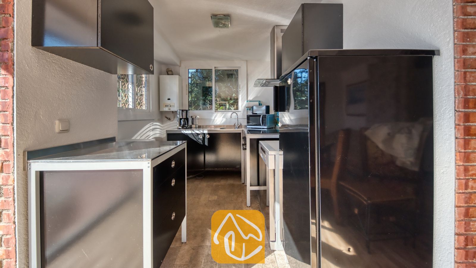 Vakantievilla's Costa Brava Spanje - Villa Gabriella - De keuken van Villa Gabriella is voorzien van zwarte kasten met witte accenten, een grote zwarte koelkast en een roestvrijstalen spoelbak onder het raam.