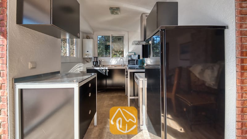 Vakantievilla's Costa Brava Spanje - Villa Gabriella - De keuken van Villa Gabriella is voorzien van zwarte kasten met witte accenten, een grote zwarte koelkast en een roestvrijstalen spoelbak onder het raam.