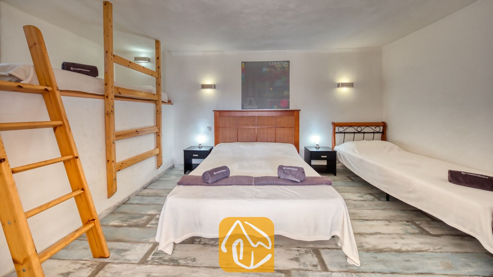 Vakantievilla's Costa Brava Spanje - Villa Gabriella - Slaapkamer in Villa Gabriella met een tweepersoonsbed, een eenpersoonsbed en een ingebouwd stapelbed. De kamer is voorzien van houten hoofdborden, paarse handdoeken en een lichte, verweerde vloer.