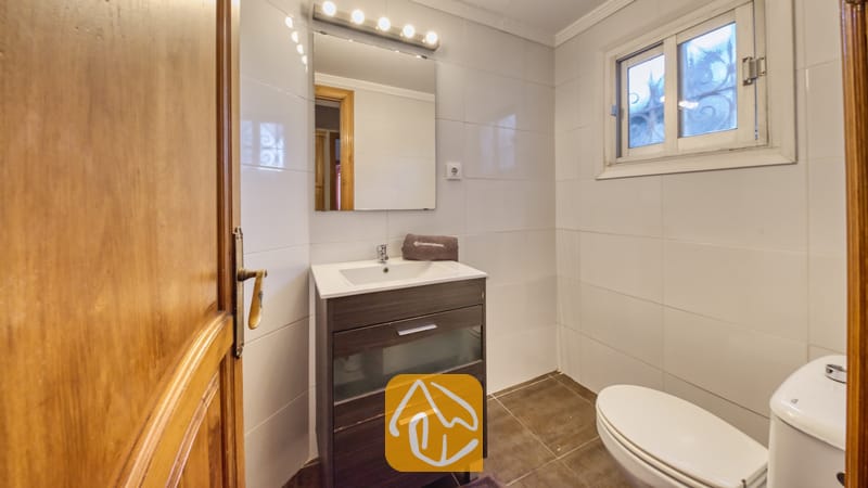 Holiday villas Costa Brava Spain - Villa Abigail - Bathroom with a dark wood vanity, white tiled walls, square mirror with five lights, and a white toilet.