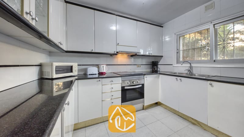 Holiday villas Costa Brava Spain - Villa Abigail - Kitchen with white gloss cabinets, black granite countertops, stainless steel oven, and a window with security bars.