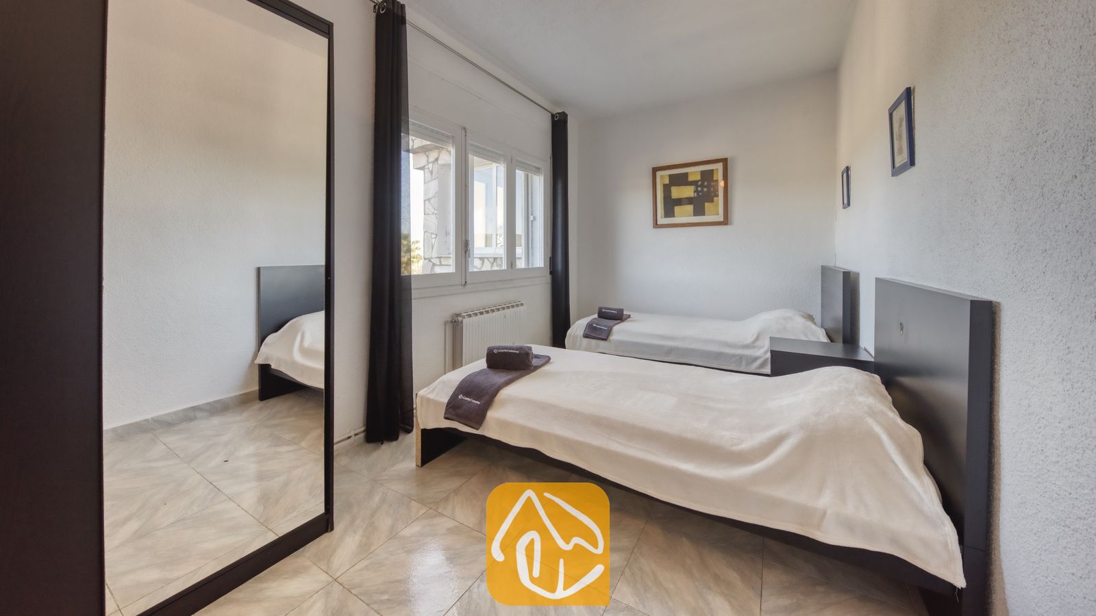 Vakantievilla's Costa Brava Spanje - Villa Abigail - Tweepersoonskamer met twee eenpersoonsbedden bij Villa Abigail, voorzien van wit beddengoed, donkere hoofdborden, een grote passpiegel, tegelvloeren en ingelijste wanddecoratie.
