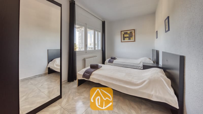 Holiday villas Costa Brava Spain - Villa Abigail - Twin bedroom at Villa Abigail featuring two single beds with white linens, dark headboards, a large floor mirror, tiled flooring, and framed wall art.
