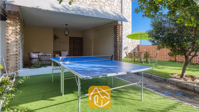 Vakantievilla's Costa Brava Spanje - Villa Abigail - Een blauwe tafeltennistafel op het kunstgras van Villa Abigail, voorzien van een overdekt terras en een eethoek buiten met een groene parasol.
