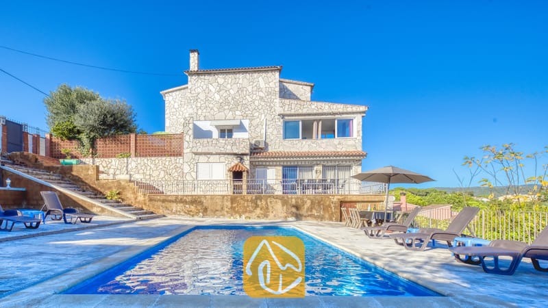 Vakantievilla's Costa Brava Spanje - Villa Abigail - Rechthoekig zwembad voor de stenen buitengevel van Villa Abigail onder een helderblauwe hemel, voorzien van ligstoelen rondom en een parasol.