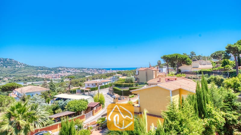 Holiday villas Costa Brava Spain - Villa Abigail - Elevated view from Villa Abigail overlooking residential hills, terracotta tile rooftops, lush green trees, and the distant blue sea under a clear sky.