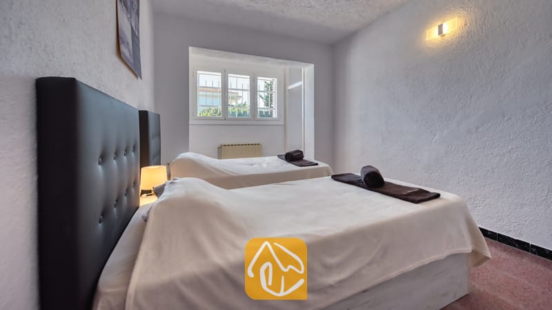 Holiday villas Costa Brava Spain - Villa Abigail - Bedroom with two single beds featuring dark tufted headboards, white linens, and rolled dark towels under a small window.