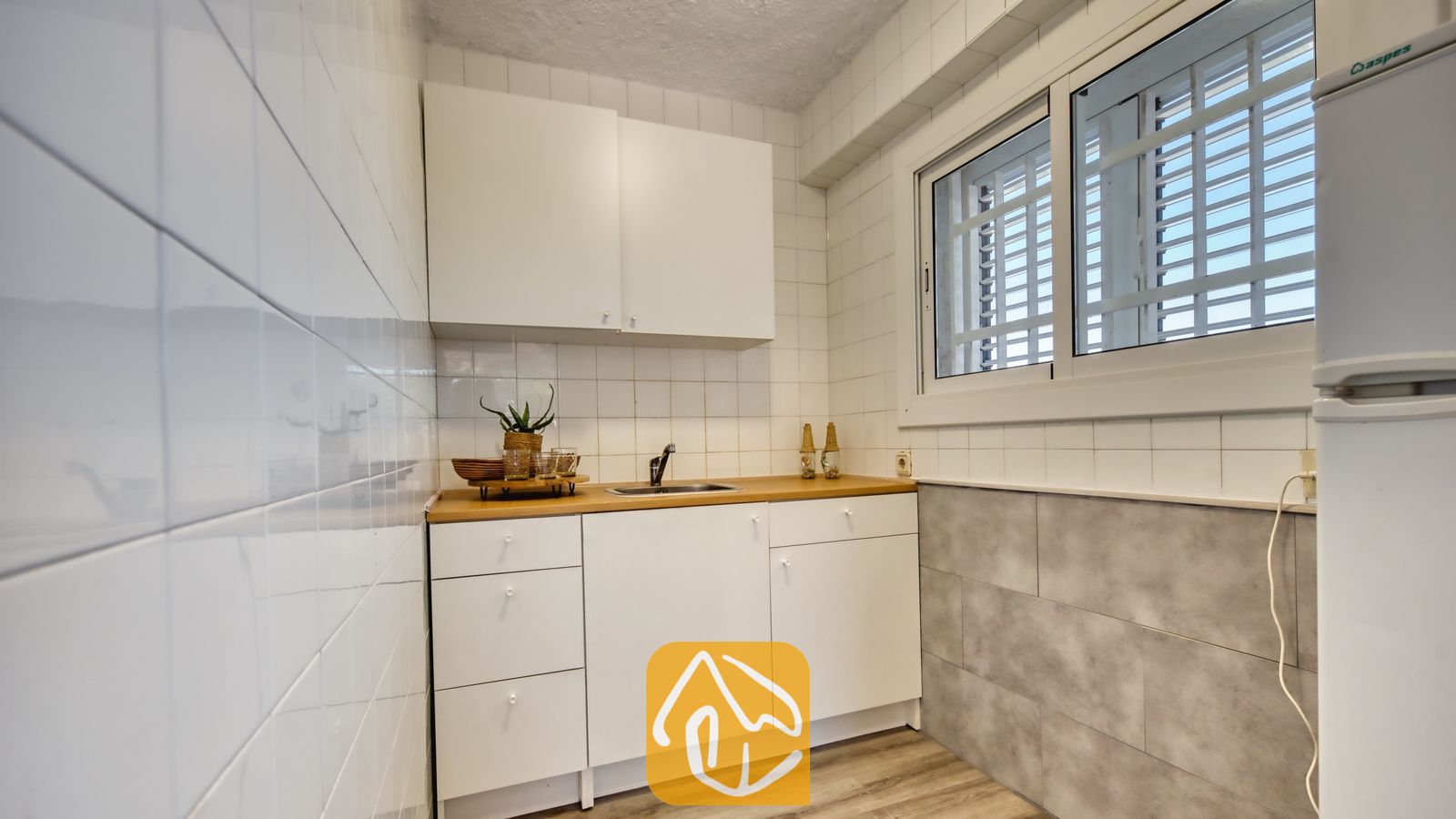 Vakantievilla's Costa Brava Spanje - Villa Abigail - Kleine kitchenette met witte kasten, een houten aanrechtblad en een raam met dievenijzers.