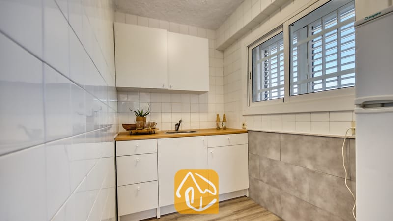 Holiday villas Costa Brava Spain - Villa Abigail - Small kitchen corner featuring white cabinets, a wooden countertop, and a window with security bars.