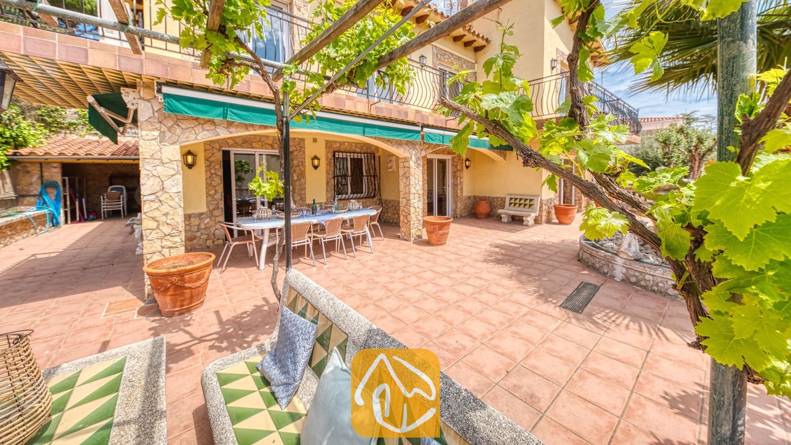 Vakantievilla's Costa Brava Spanje - Villa Dolce Vita - Zonnig terras bij Villa Dolce Vita met een betegelde eettafel buiten, stenen zuilen en overkapping van klimmende druivenranken