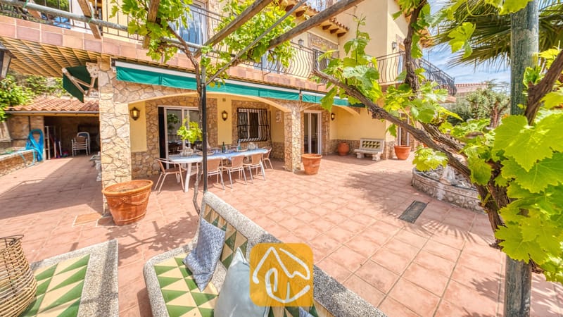 Vakantievilla's Costa Brava Spanje - Villa Dolce Vita - Zonnig terras bij Villa Dolce Vita met een betegelde eettafel buiten, stenen zuilen en overkapping van klimmende druivenranken
