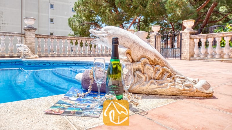 Vakantievilla's Costa Brava Spanje - Villa Dolce Vita - Fles champagne en twee glazen op een betegeld zwembadterras naast een stenen dolfijnenstandbeeld bij Villa Dolce Vita