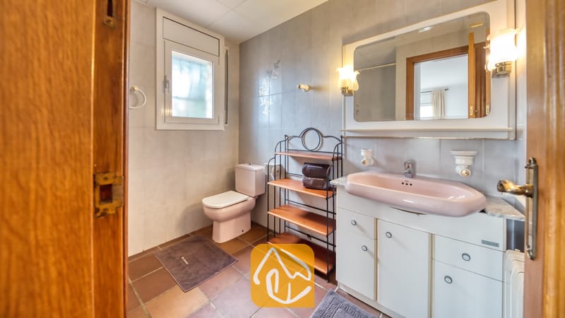 Villas de vacances Costa Brava Espagne - Villa Dolce Vita - Salle de bains comprenant un meuble sous-lavabo rose, des toilettes assorties, des murs carrelés et une étagère en métal à plateaux en bois