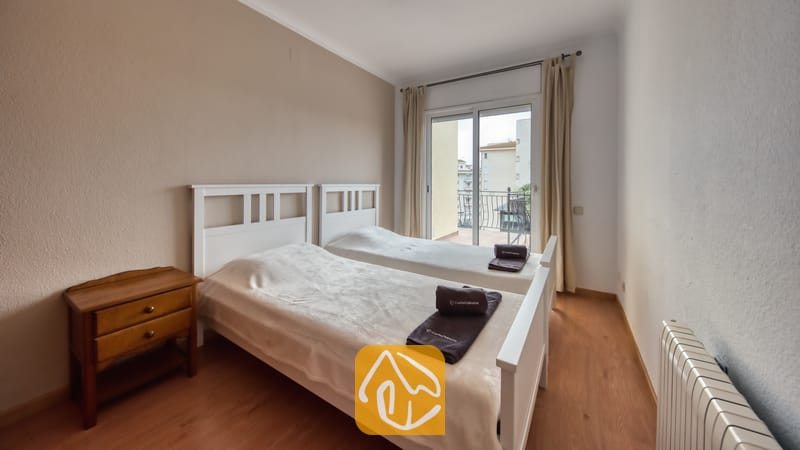 Villas de vacances Costa Brava Espagne - Villa Dolce Vita - Chambre avec deux lits jumeaux blancs, une table de chevet en bois et des portes coulissantes en verre s'ouvrant sur un balcon.