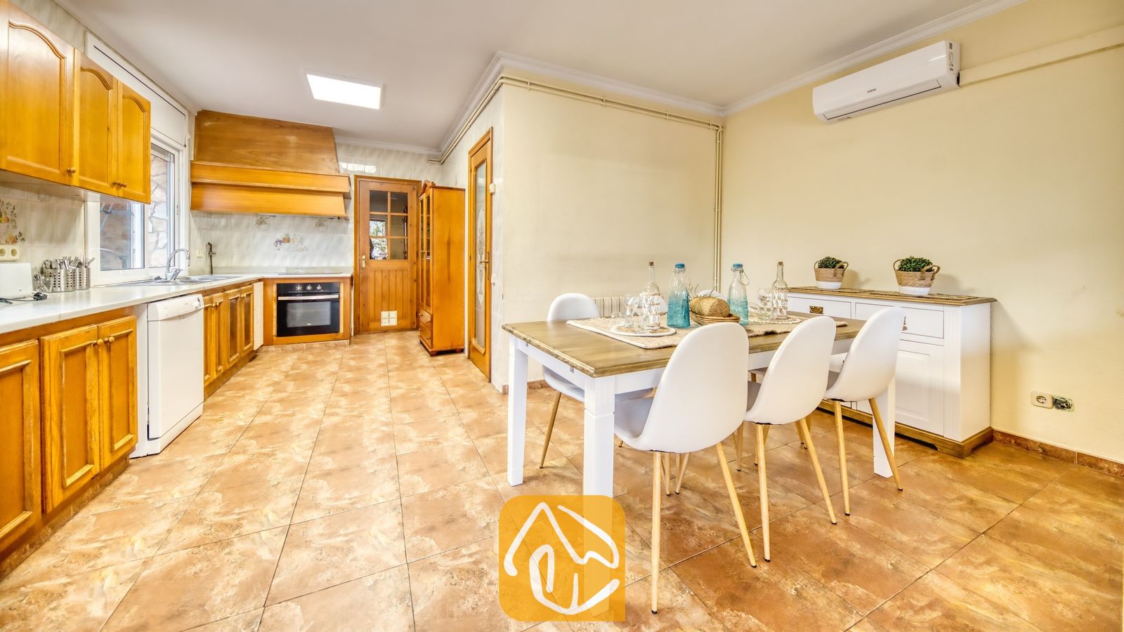 Vakantievilla's Costa Brava Spanje - Villa Dolce Vita - Keuken en eetgedeelte met een houten eettafel met witte stoelen, houten kasten en tegelvloeren in Villa Dolce Vita.