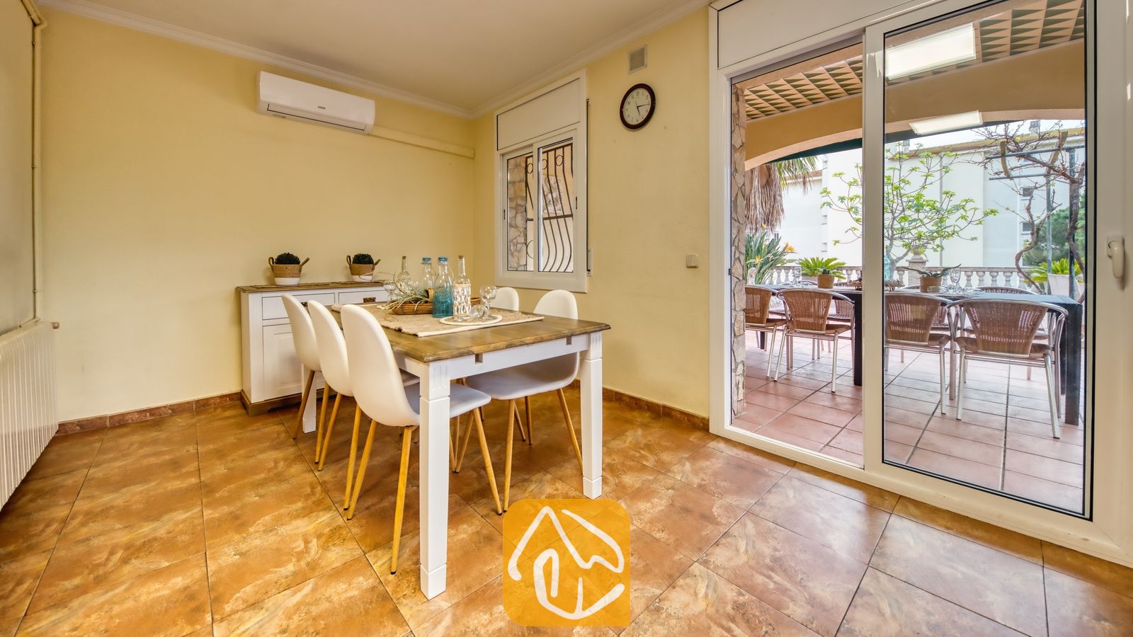 Vakantievilla's Costa Brava Spanje - Villa Dolce Vita - Eethoek met een houten tafel, witte stoelen en glazen flessen, die via schuifdeuren toegang biedt tot een buitenterras bij Villa Dolce Vita.