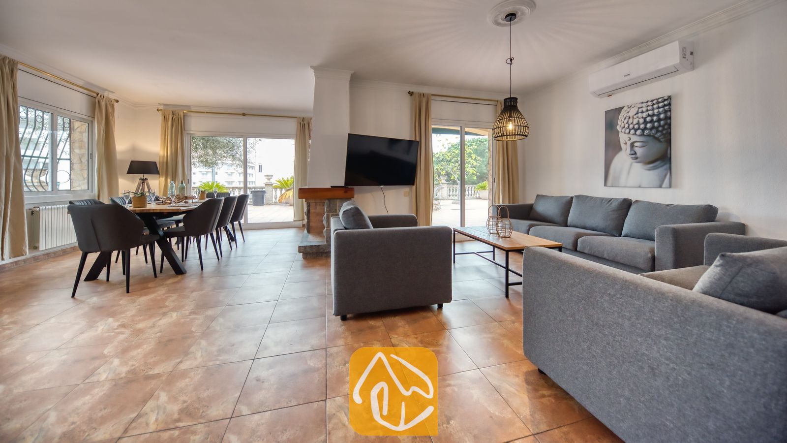 Vakantievilla's Costa Brava Spanje - Villa Dolce Vita - Ruime woon- en eetkamer in Villa Dolce Vita met grijs stoffen banken, een houten eettafel met zwarte stoelen en grote glazen deuren die opengaan naar een terras.