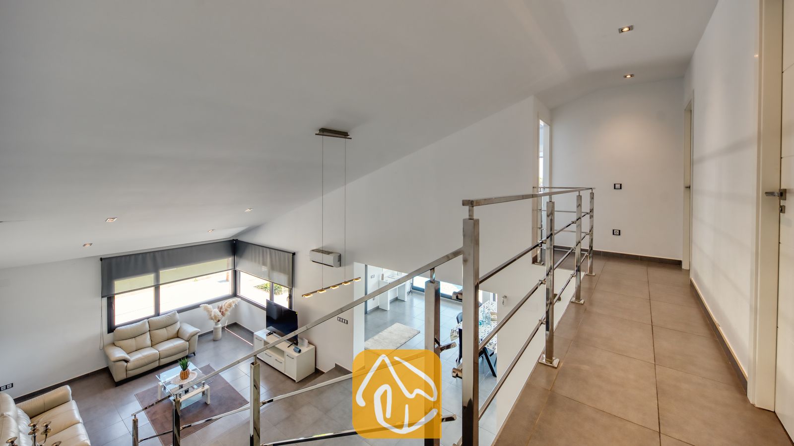 Vakantievilla's Costa Brava Spanje - Villa SummerDream - Bovenste gang van Villa SummerDream met uitzicht op de benedenverdieping met betegelde vloeren, een metalen balustrade en witte muren onder een schuin plafond.