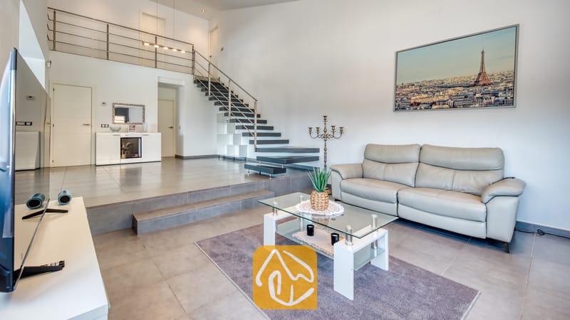 Vakantievilla's Costa Brava Spanje - Villa SummerDream - Ruime woonkamer in Villa SummerDream, voorzien van een grijze leren bank, een glazen salontafel op een paars vloerkleed en een open trap met metalen leuningen.