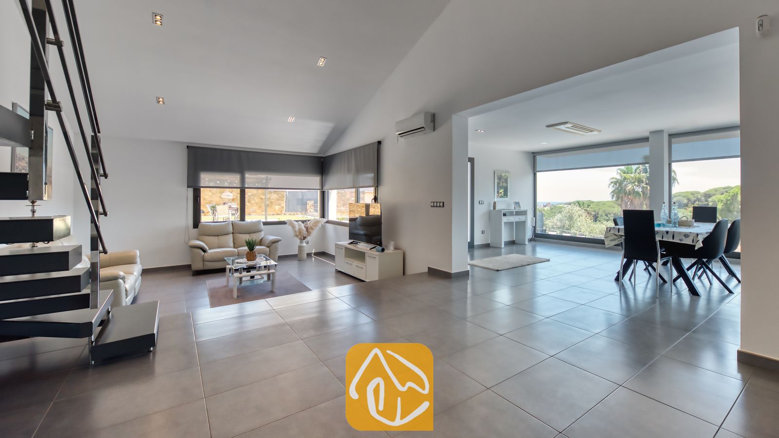 Vakantievilla's Costa Brava Spanje - Villa SummerDream - Ruime, open woonkamer in Villa SummerDream met grijze tegelvloer, witte muren, een leren bank en een aangrenzende eethoek met grote ramen.