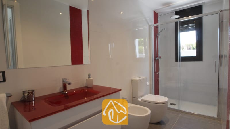 Villas de vacances Costa Brava Espagne - Villa SummerDream - Salle de bains moderne dotée d'une vasque sur plan de travail rouge, d'un meuble sous-lavabo blanc, d'une douche fermée par une paroi en verre, ainsi que de toilettes et d'un bidet blancs assortis, le tout complété par des murs aux accents blancs et rouges.