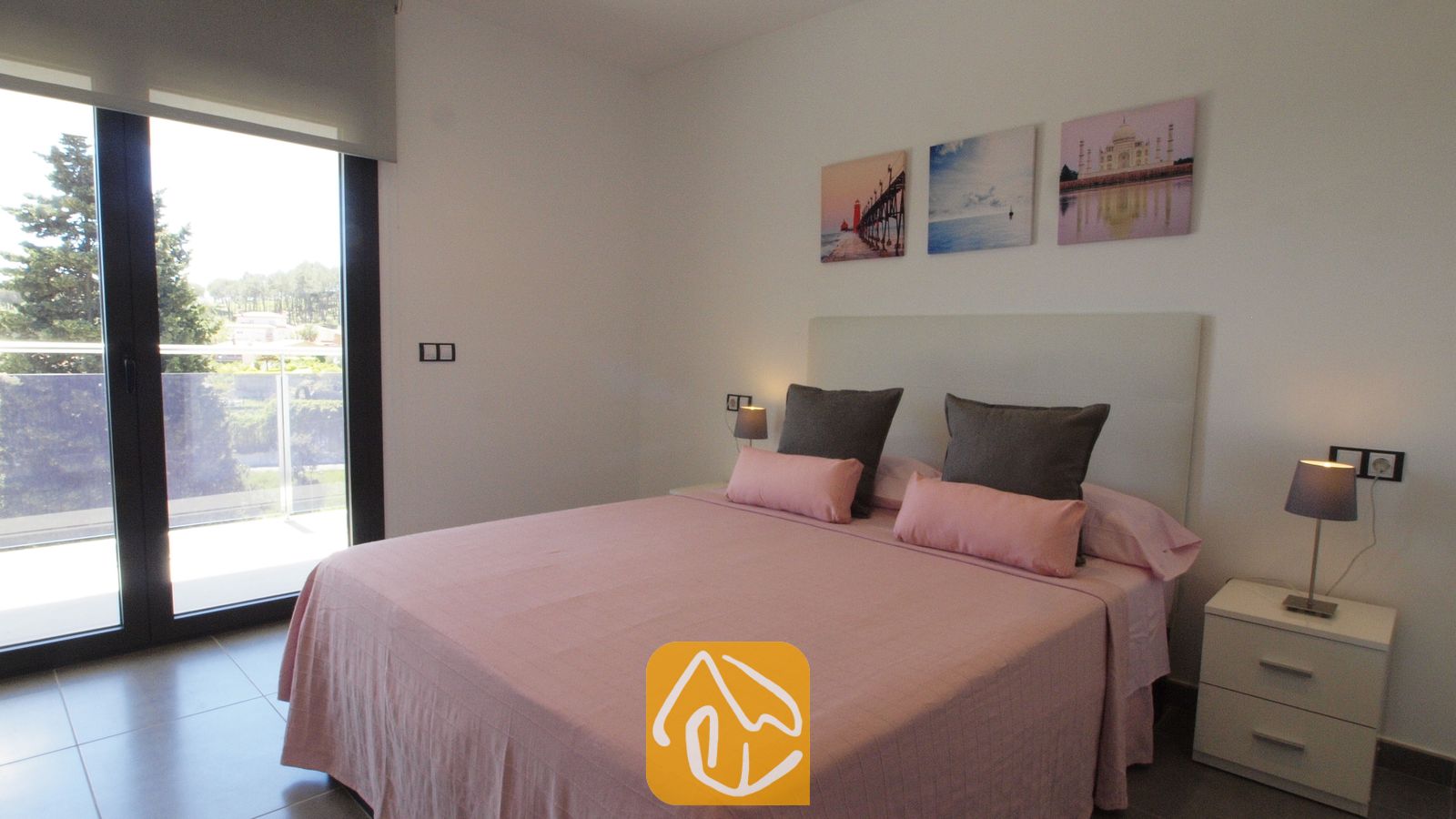 Vakantievilla's Costa Brava Spanje - Villa SummerDream - Slaapkamer met roze beddengoed, donkergrijze kussens, twee witte nachtkastjes met kleine lampen en een glazen schuifdeur die toegang biedt tot een buitenbalkon.