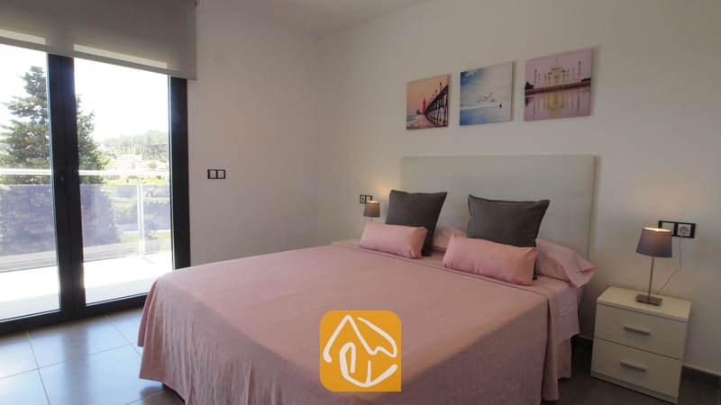 Villas de vacances Costa Brava Espagne - Villa SummerDream - Chambre avec parure de lit rose, oreillers gris foncé, deux tables de chevet blanches surmontées de petites lampes, et une porte coulissante en verre donnant sur un balcon extérieur.