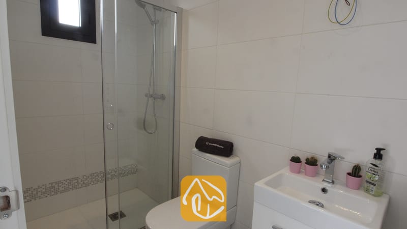 Villas de vacances Costa Brava Espagne - Villa SummerDream - Salle de bain moderne dotée d'une douche à l'italienne avec porte en verre, de murs carrelés de blanc, de toilettes surmontées d'une serviette sombre enroulée, ainsi que d'un lavabo blanc agrémenté de petits cactus roses en pot.