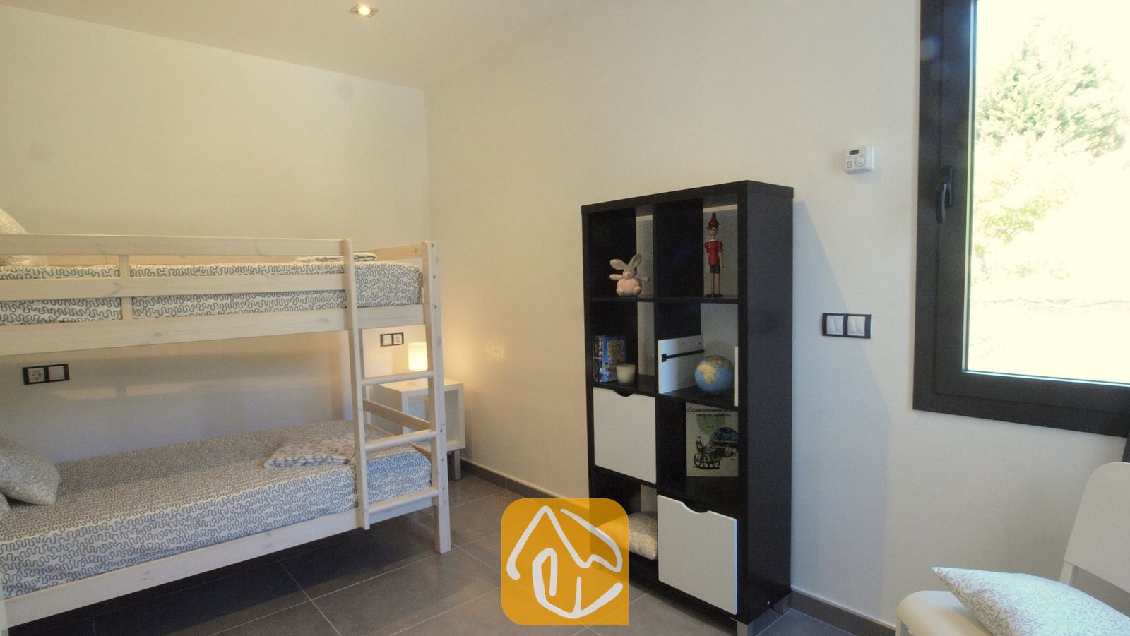 Vakantievilla's Costa Brava Spanje - Villa SummerDream - Slaapkamer met houten stapelbed, een zwart wandrek met speelgoed en boeken, en een raam met uitzicht op groen loof.