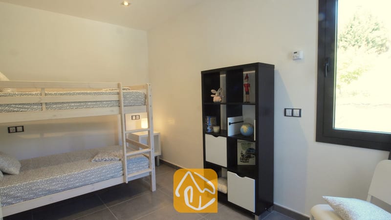 Villas de vacances Costa Brava Espagne - Villa SummerDream - Chambre avec des lits superposés en bois, une étagère noire remplie de jouets et de livres, et une fenêtre offrant une vue sur un feuillage verdoyant.