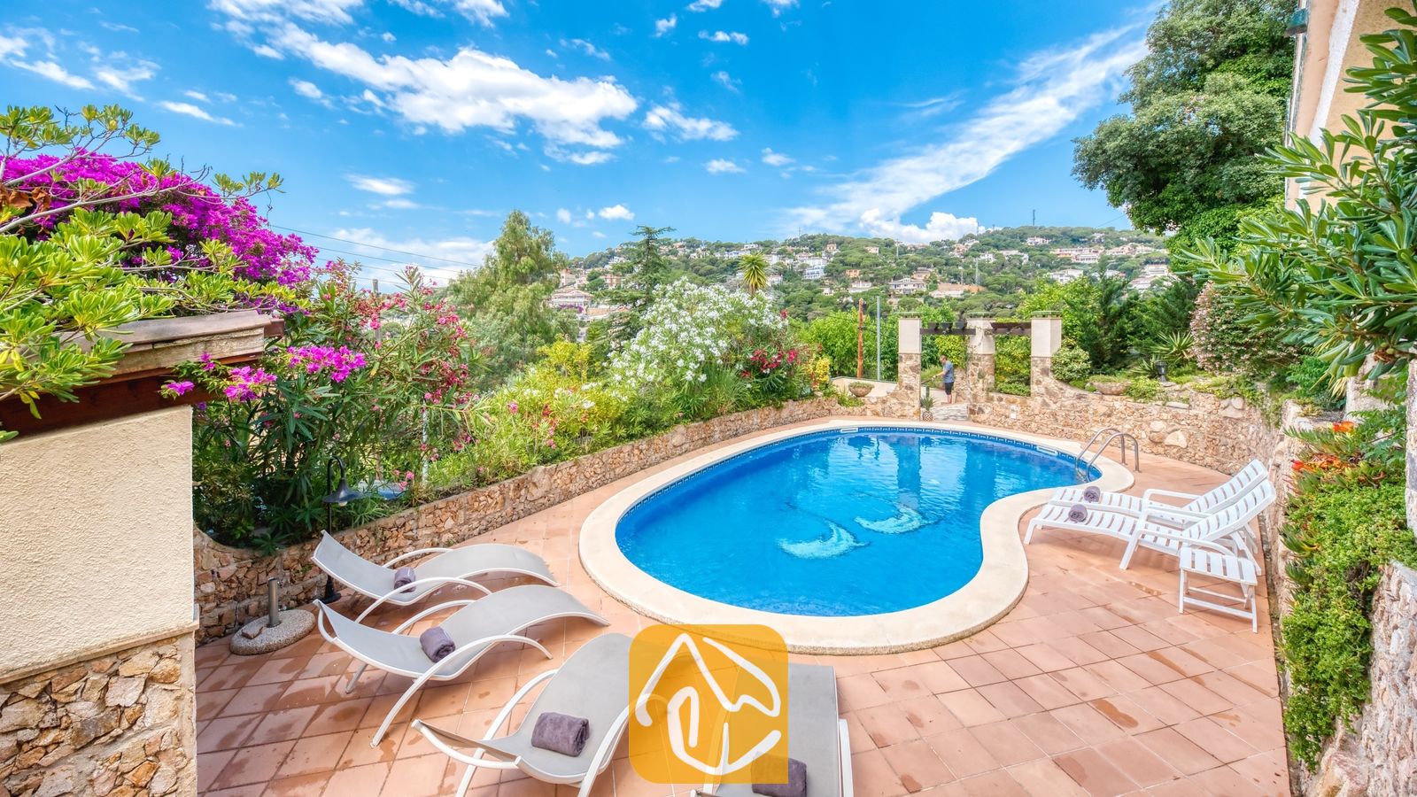 Vakantievilla's Costa Brava Spanje - Villa Cleo - Privézwembad met ligstoelen en betegeld terras bij Villa Cleo in Spanje, omringd door stenen muren en bloeiende struiken.