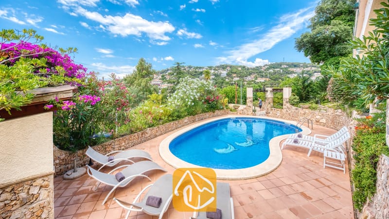 Vakantievilla's Costa Brava Spanje - Villa Cleo - Privézwembad met ligstoelen en betegeld terras bij Villa Cleo in Spanje, omringd door stenen muren en bloeiende struiken.