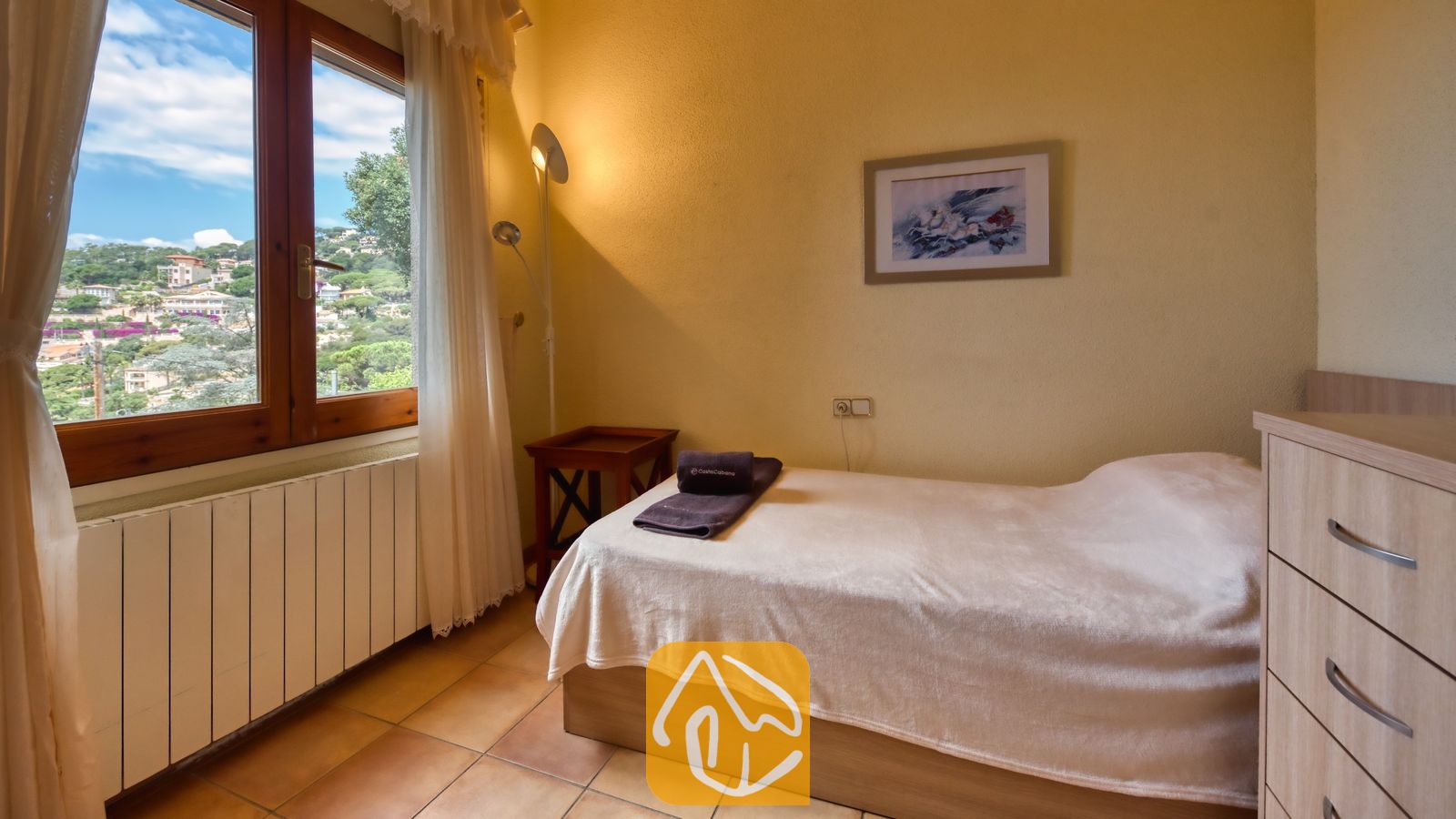 Vakantievilla's Costa Brava Spanje - Villa Cleo - Slaapkamer met een eenpersoonsbed, witte muren, houten kozijnen met uitzicht op de buitenheuvels en een tegelvloer.