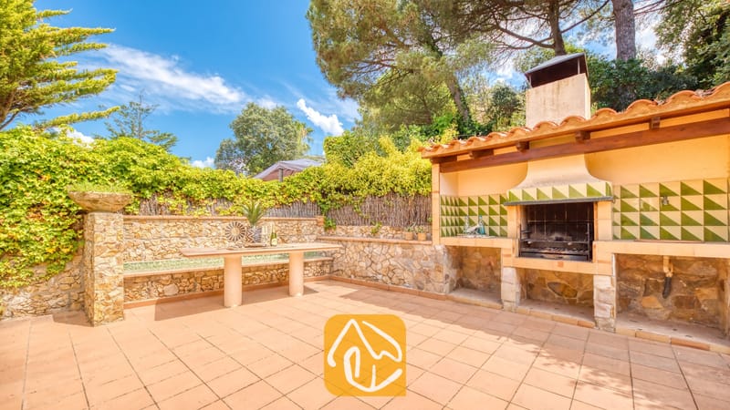 Vakantievilla's Costa Brava Spanje - Villa Cleo - Buitenbarbecuezone bij Villa Cleo met een ingebouwde stenen barbecue met groen-gepatineerde tegels, stenen muren en een betarte tuintafel.