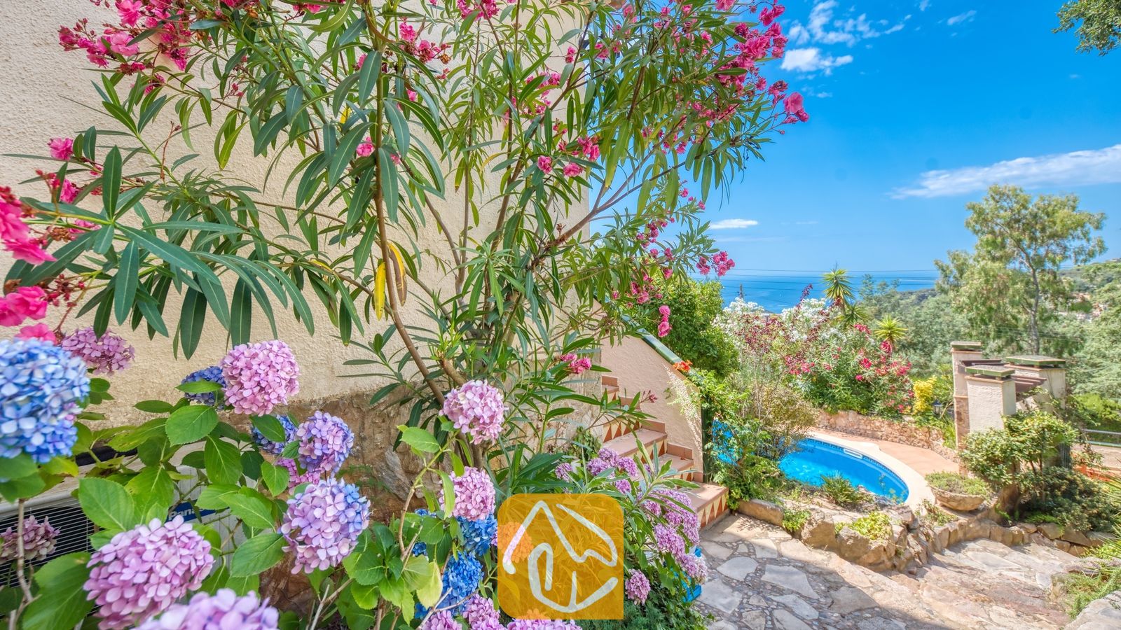 Vakantievilla's Costa Brava Spanje - Villa Cleo - Roze en blauwe hortensia's en bloeiende oleanderstruiken omlijsten een stenen buitentrap die naar beneden leidt richting het zwembad in de tuin bij Villa Cleo.