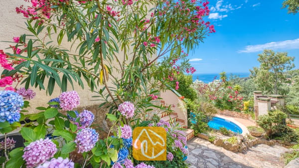 Vakantievilla's Costa Brava Spanje - Villa Cleo - Roze en blauwe hortensia's en bloeiende oleanderstruiken omlijsten een stenen buitentrap die naar beneden leidt richting het zwembad in de tuin bij Villa Cleo.