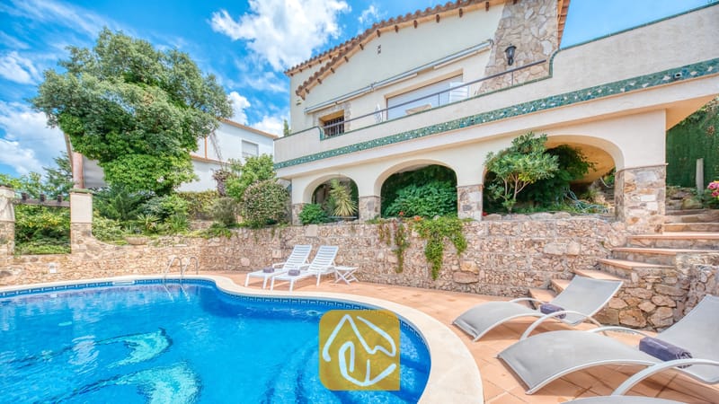 Vakantievilla's Costa Brava Spanje - Villa Cleo - Privézwembad met helderblauw water en ligbedden op het bestrate terras voor Villa Cleo, voorzien van een stenen keermuur en een benedenverdieping met bogen.