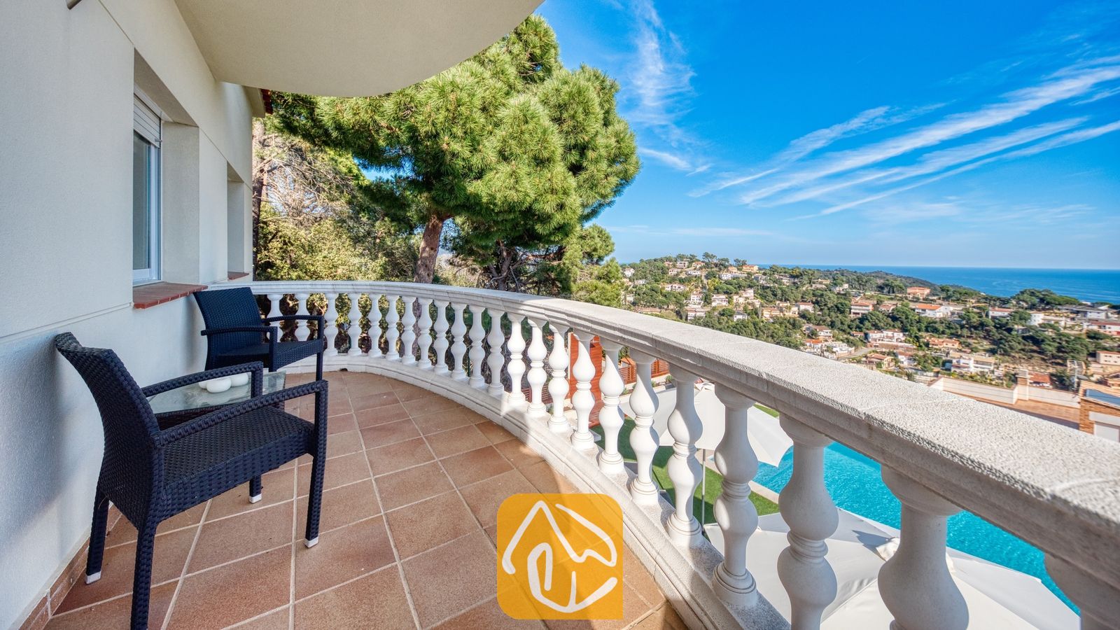 Vakantievilla's Costa Brava Spanje - Villa Chanel - Gebogen balkon bij Villa Chanel, voorzien van zwart vlechtwerkmeubilair, een witstenen balustrade en uitzicht op de kustplaats en de zee.