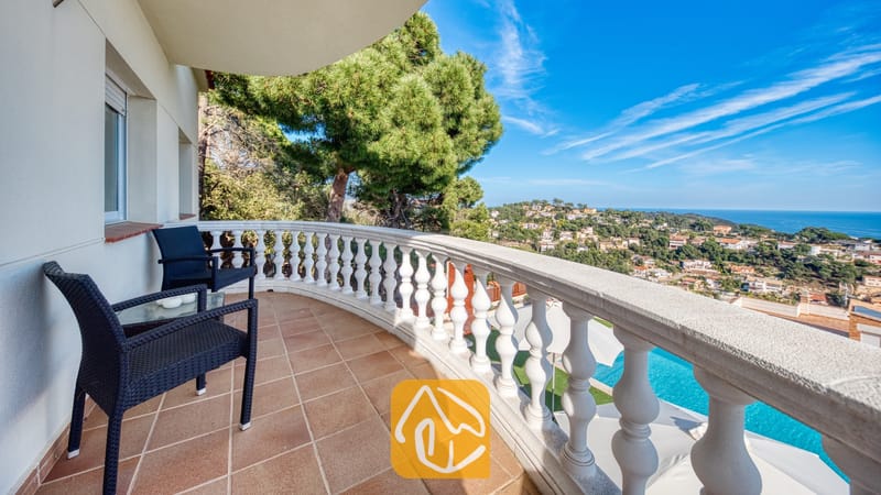 Villas de vacances Costa Brava Espagne - Villa Chanel - Balcon incurvé à la Villa Chanel, agrémenté d'un salon en osier noir, d'une balustrade en pierre blanche et offrant une vue imprenable sur la ville côtière et la mer.