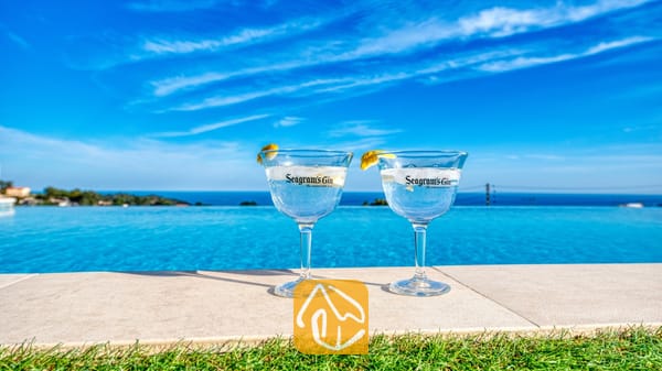 Vakantievilla's Costa Brava Spanje - Villa Chanel - Twee gin-cocktails met citroengarnituur aan de rand van het overloopzwembad van Villa Chanel, met uitzicht op de blauwe zee en de lucht.