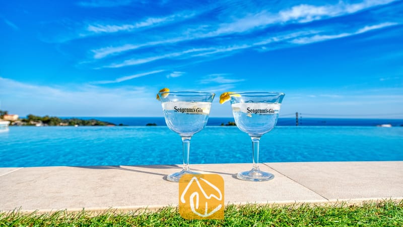 Vakantievilla's Costa Brava Spanje - Villa Chanel - Twee gin-cocktails met citroengarnituur aan de rand van het overloopzwembad van Villa Chanel, met uitzicht op de blauwe zee en de lucht.