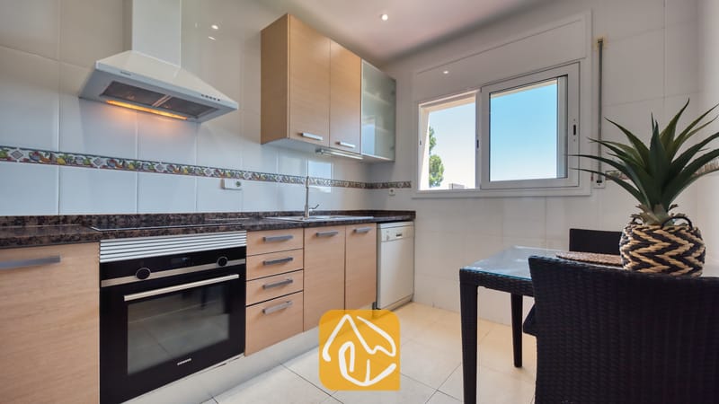 Vakantievilla's Costa Brava Spanje - Villa Chanel - De keuken van Villa Chanel is voorzien van lichthouten kasten, een zwarte Siemens-oven en een kleine eettafel met donkere rieten stoelen bij het raam.
