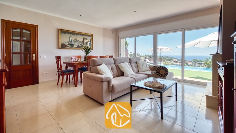 Vakantievilla's Costa Brava Spanje - Villa Chanel - Woonkamer met een beige bank en een glazen salontafel in Villa Chanel, voorzien van schuifdeuren die toegang bieden tot een terras met zwembad en uitzicht op zee.