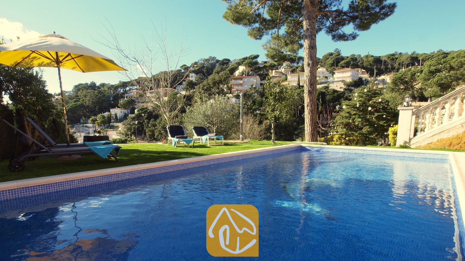 Vakantievilla's Costa Brava Spanje - Villa Noa - Privézwembad met blauwe tegelrand bij Villa Noa, voorzien van ligstoelen op het gras en uitzicht op de heuvels onder een heldere hemel.