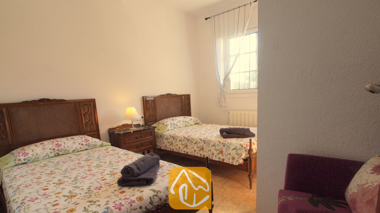 Vakantievilla's Costa Brava Spanje - Villa Noa - Slaapkamer met twee eenpersoonsbedden, voorzien van donkerhouten hoofdborden, spreien met bloemenmotief en opgerolde grijze handdoeken.