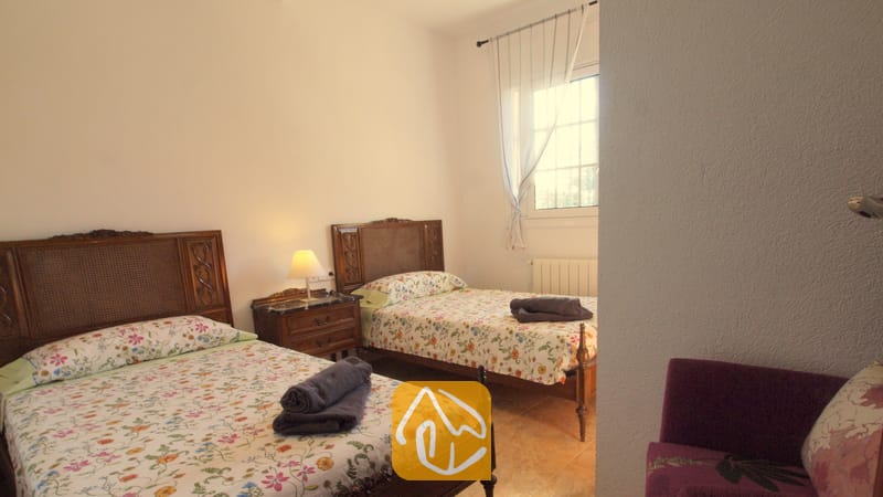 Holiday villas Costa Brava Spain - Villa Noa - Bedroom with two twin beds featuring dark wood headboards, floral patterned bedspreads, and rolled grey towels.